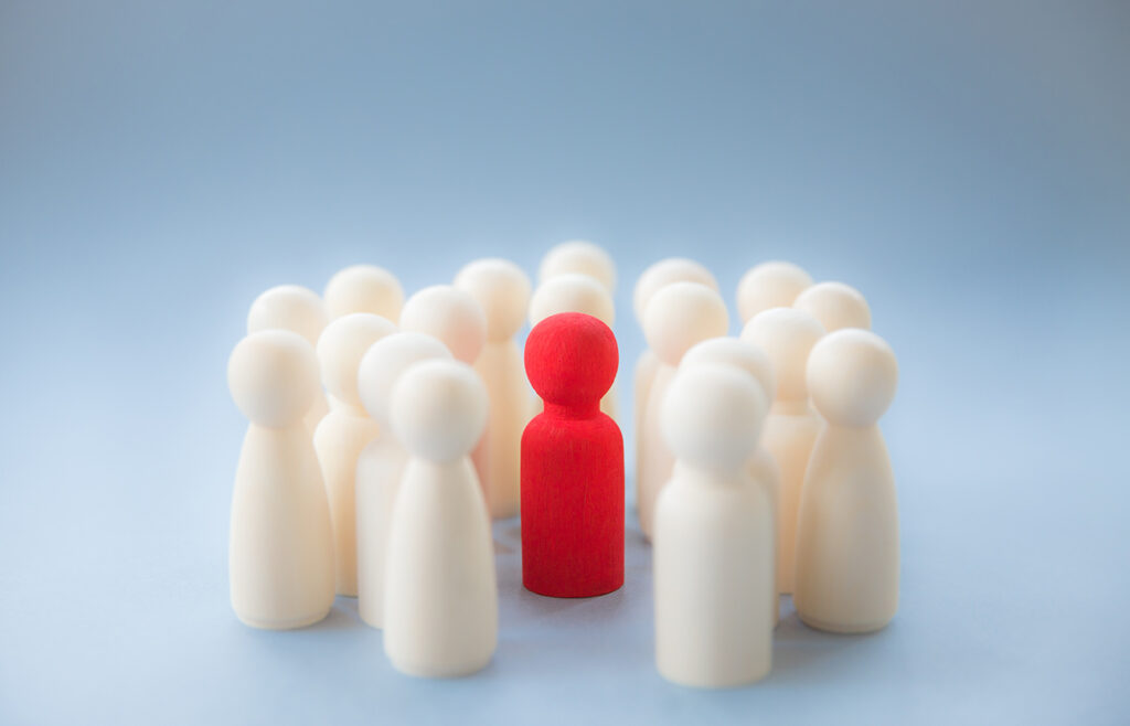 A group of little wooden figures, all white except for a red one in the center that stands out.
